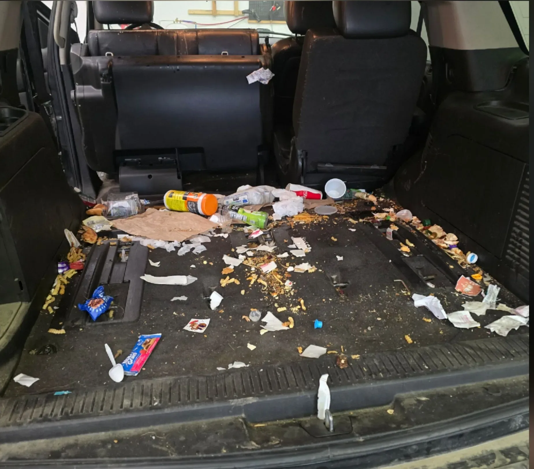 SUV cargo area filled with trash, crumbs and embedded debris before interior detailing